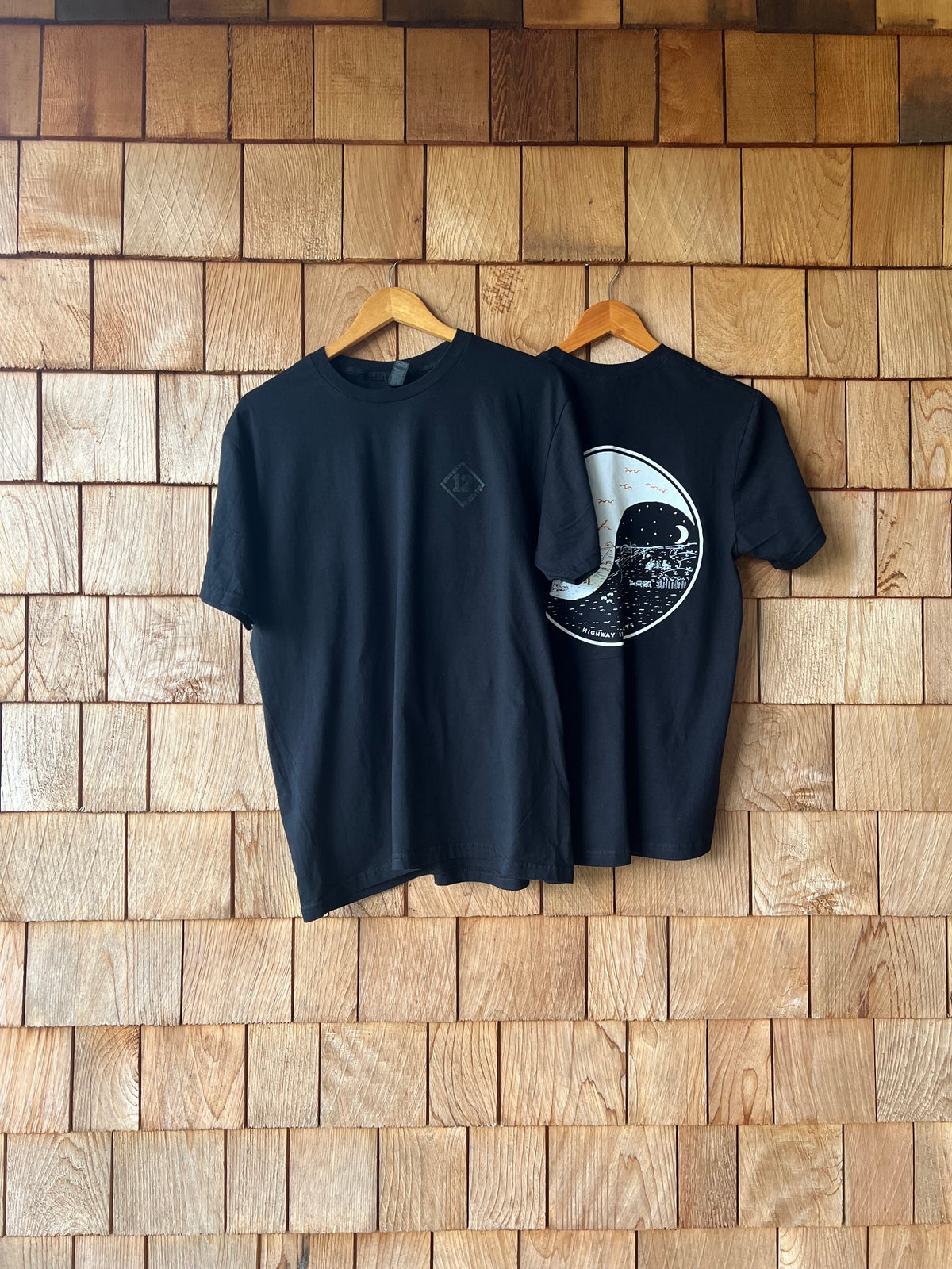 Black t-shirt with a white graphic design on a wooden wall