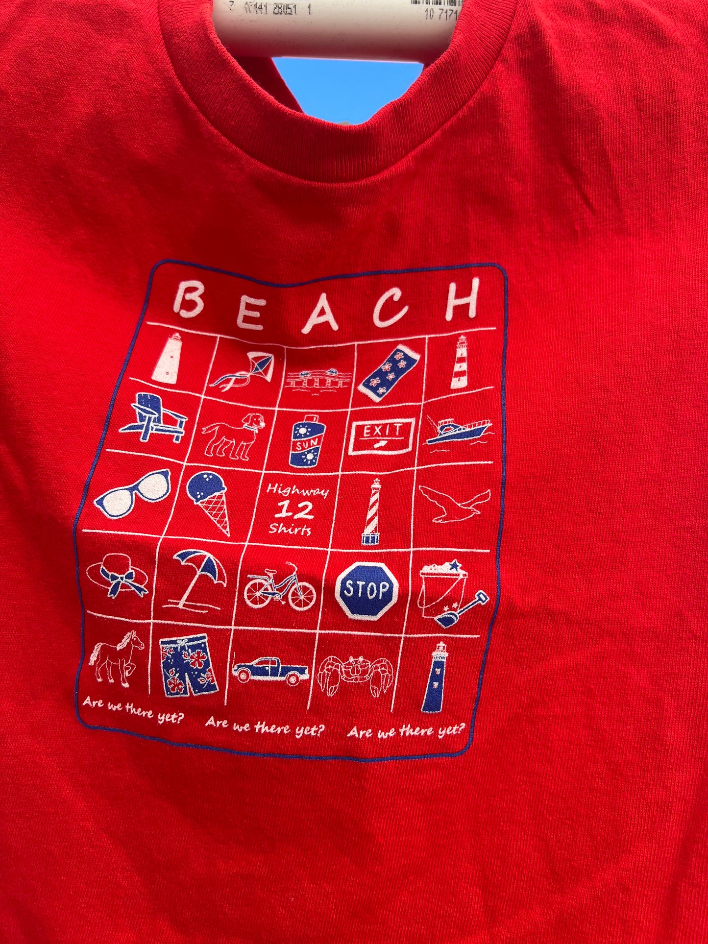 Red shirt with beach-themed graphic design on a blue background