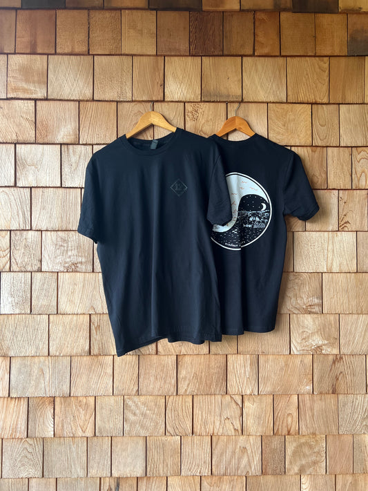 Black t-shirt with a white graphic design on a wooden wall