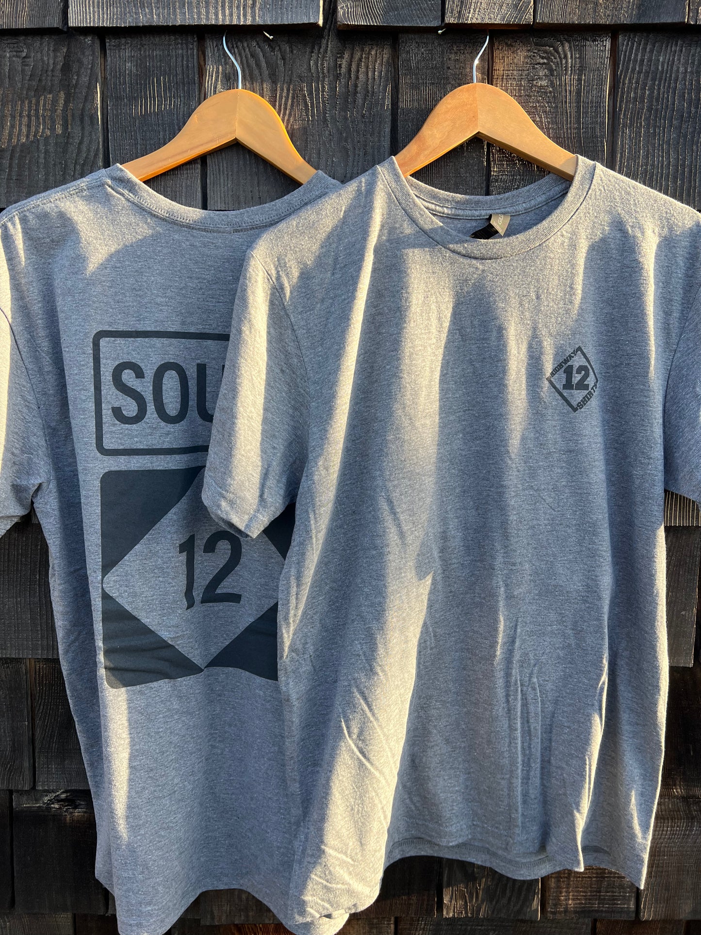 Two gray t-shirts with geometric designs on hangers against a wooden background