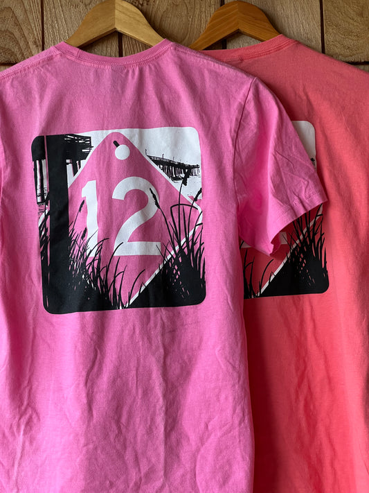Pink t-shirt with a black and white graphic design on a wooden surface