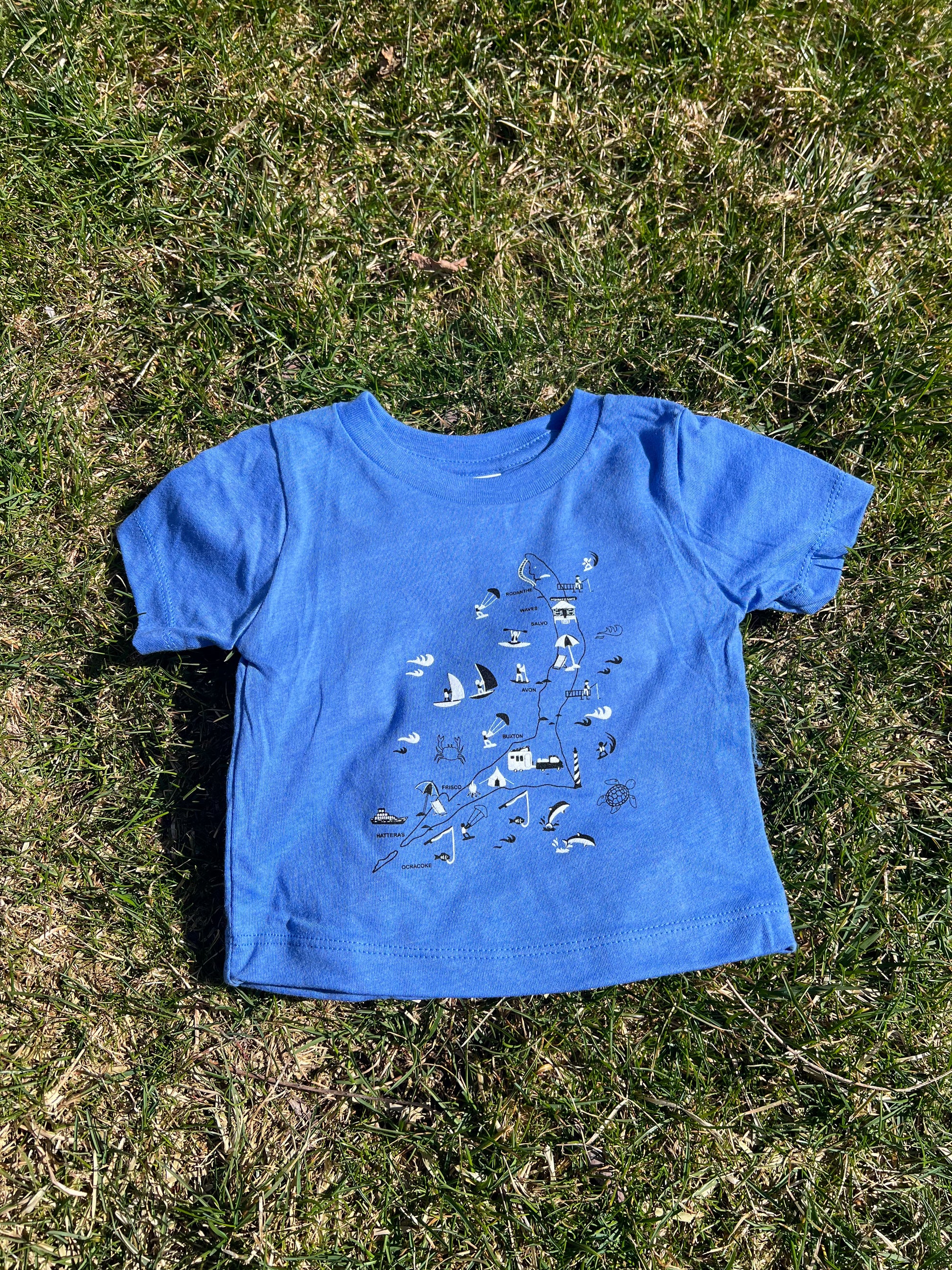 A blue infant tee with a graphic print laid out on the grass.