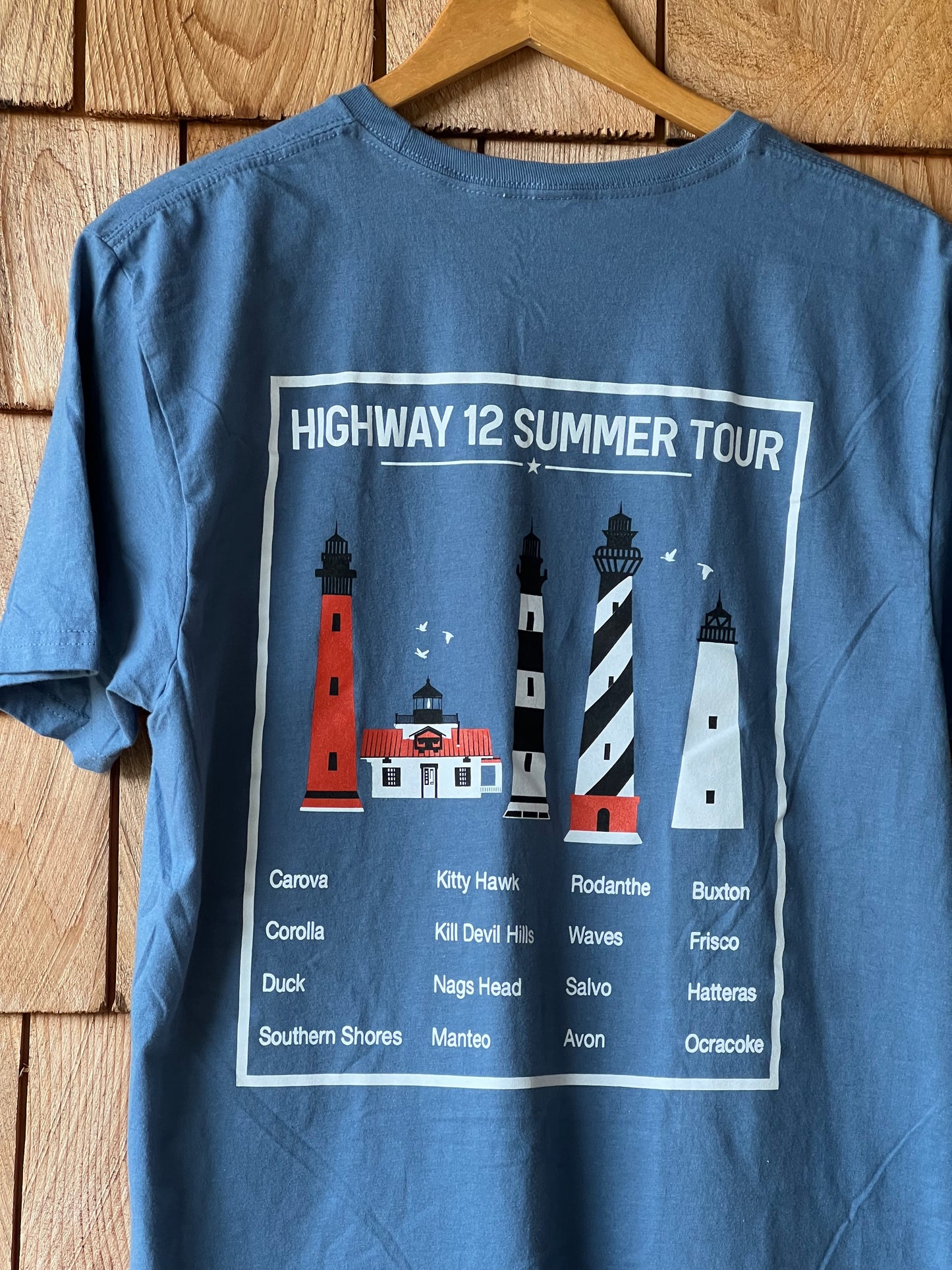 Blue short sleeve shirt with lighthouse design and text on a wooden surface