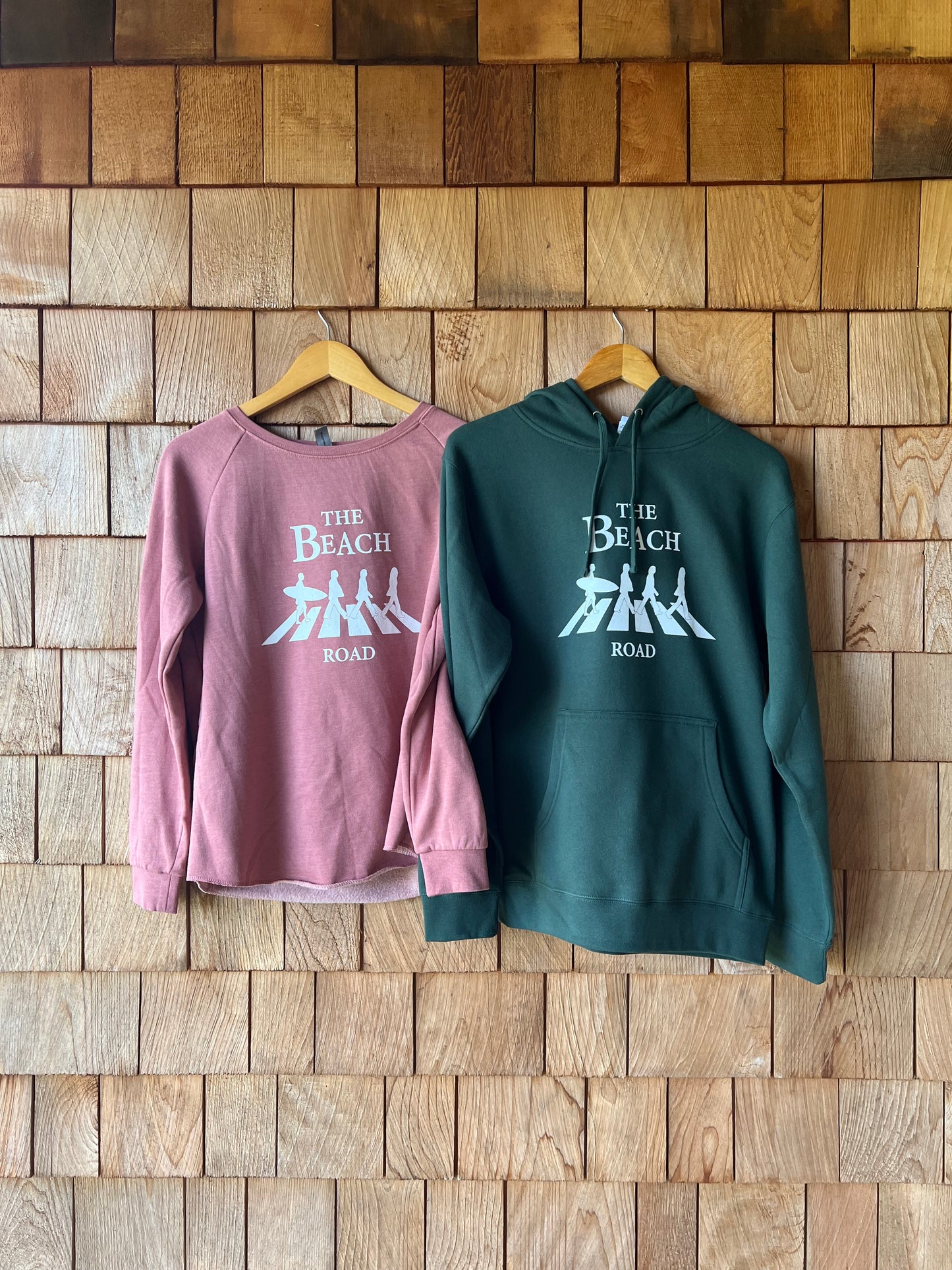Two hoodies, one green and one pink, with text on a wooden surface.
