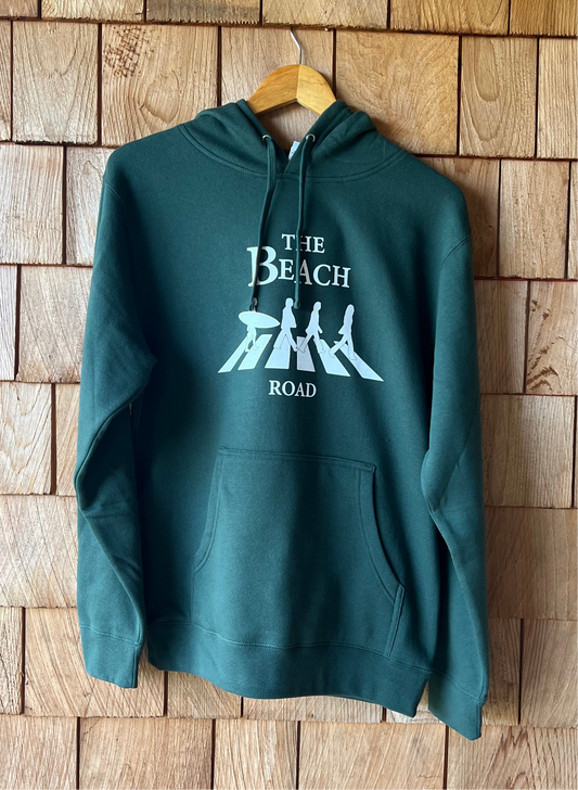 Green hoodie with 'The Beach Road' design on a wooden wall