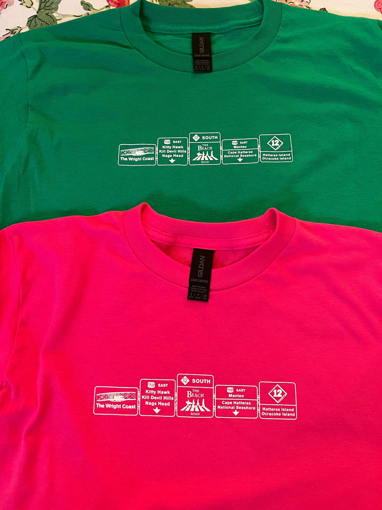 Green and pink t-shirts with white text and graphics on a floral background