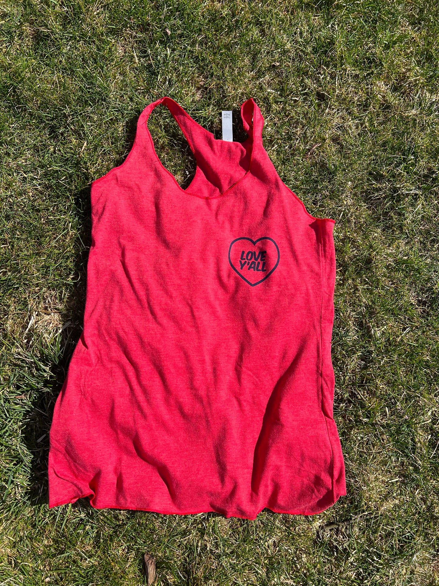 A red racerback women's tank top with a graphic on the front laying on a grassy surface.
