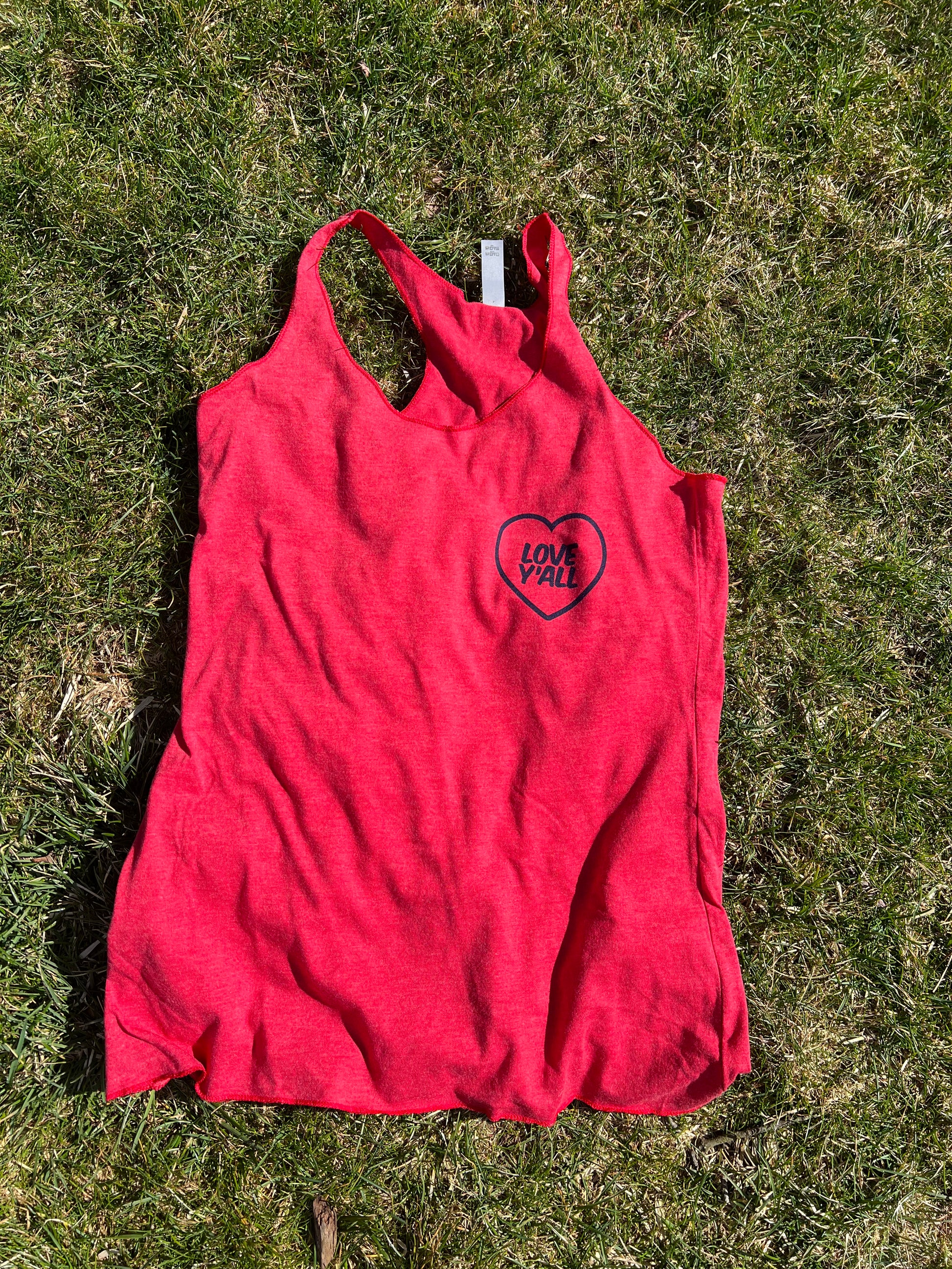 A red racerback women's tank top with a graphic on the front laying on a grassy surface.