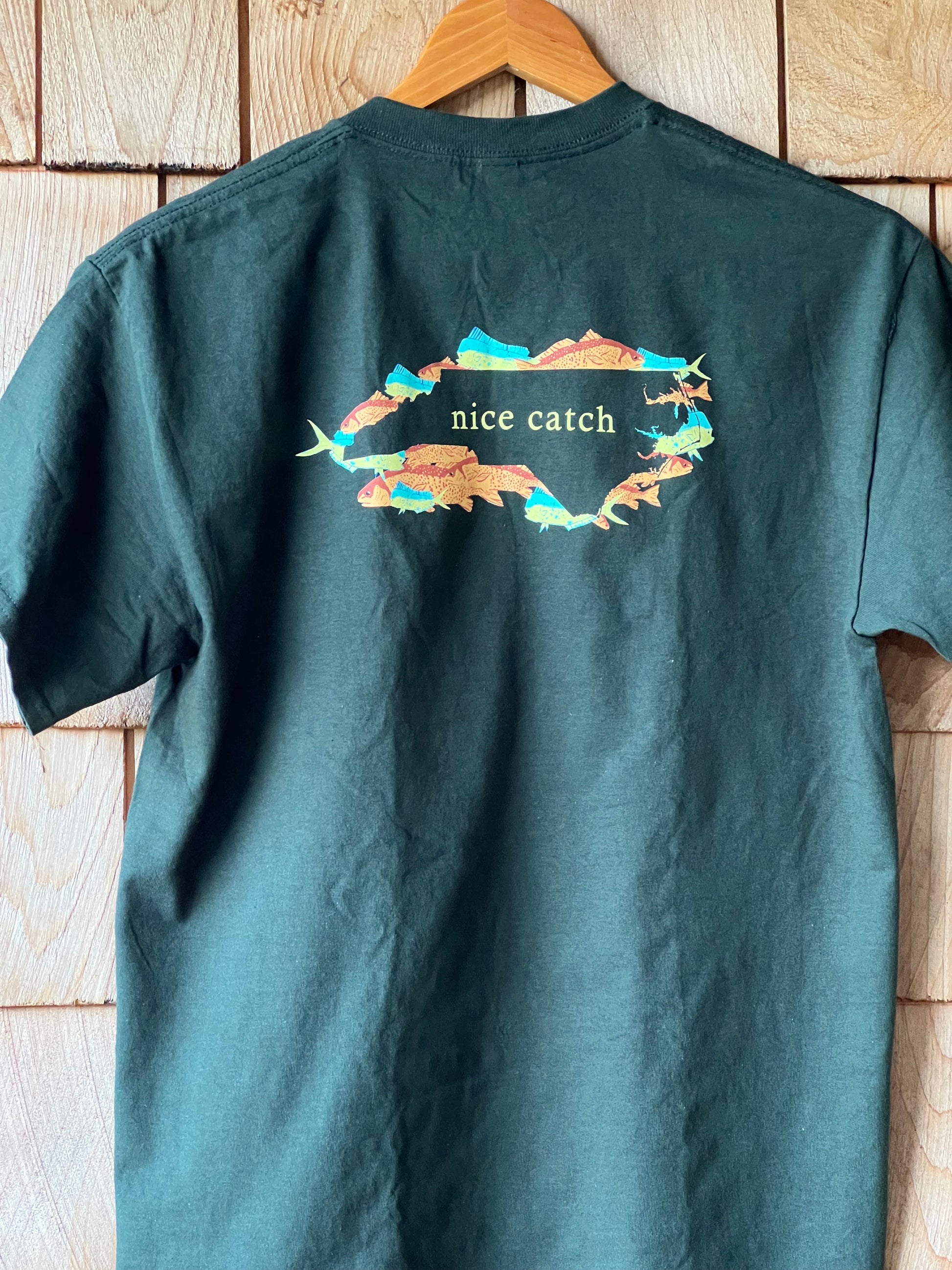 Green t-shirt with a colorful graphic and text on a wooden surface