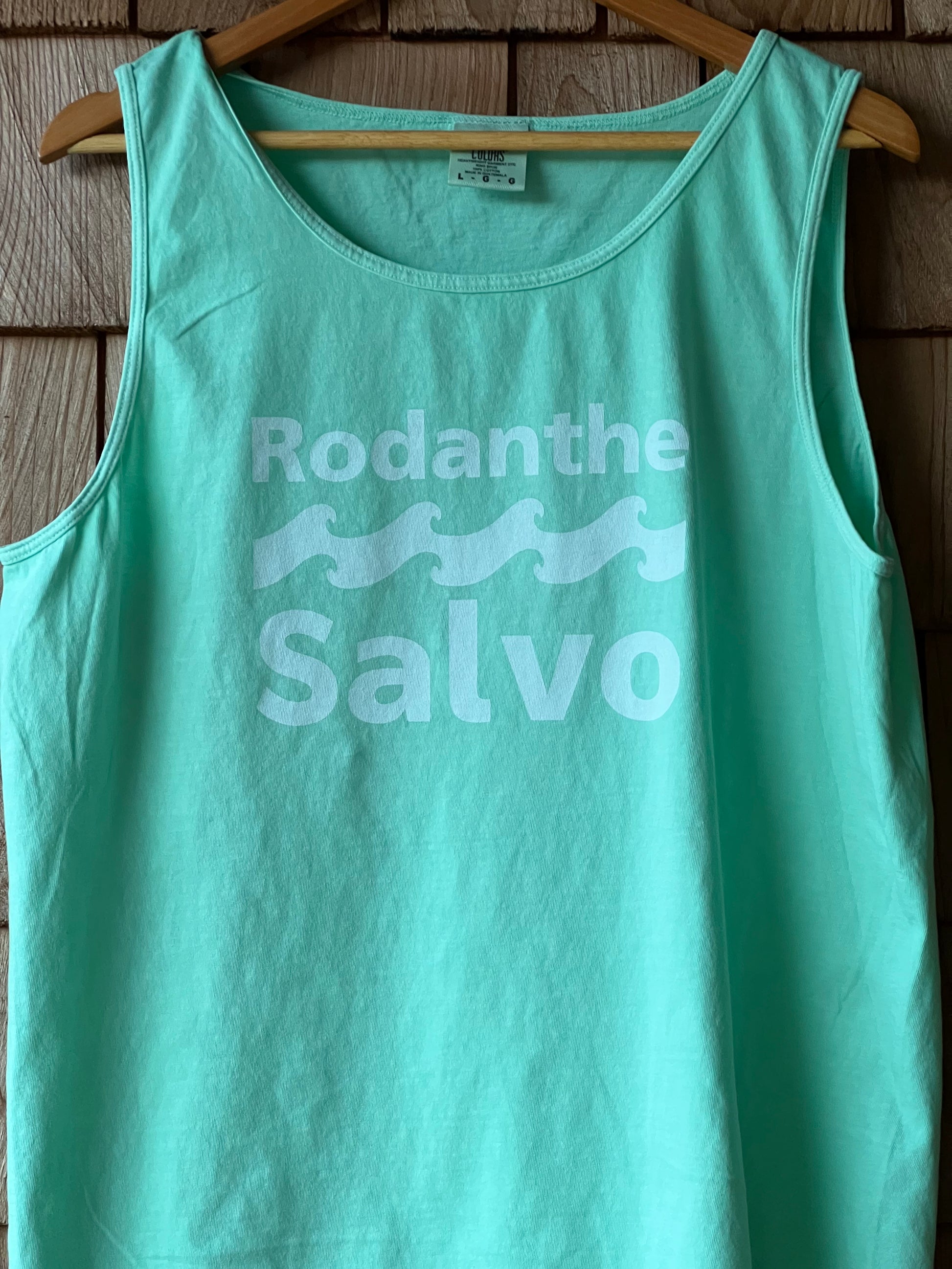 Turquoise tank top with 'Rodanthe Salvo' text on a wooden background