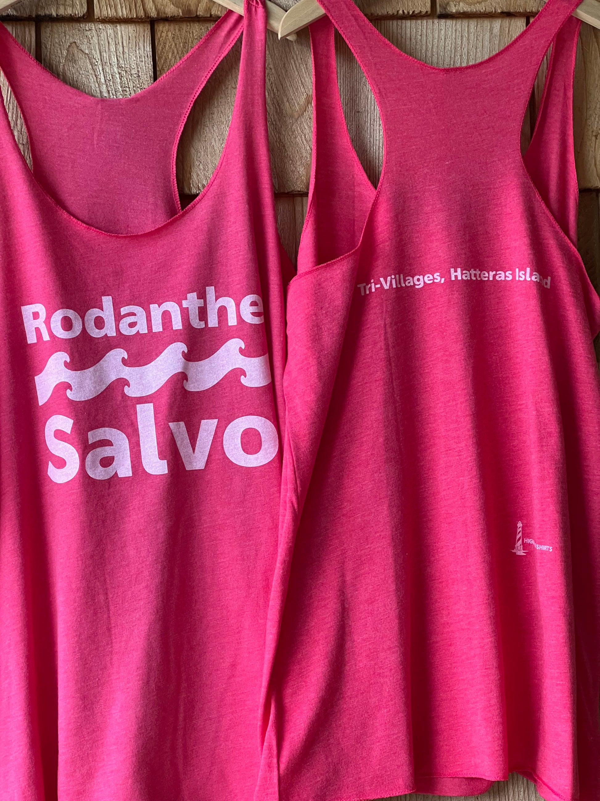 Two pink tank tops with a logo and text on a wooden surface
