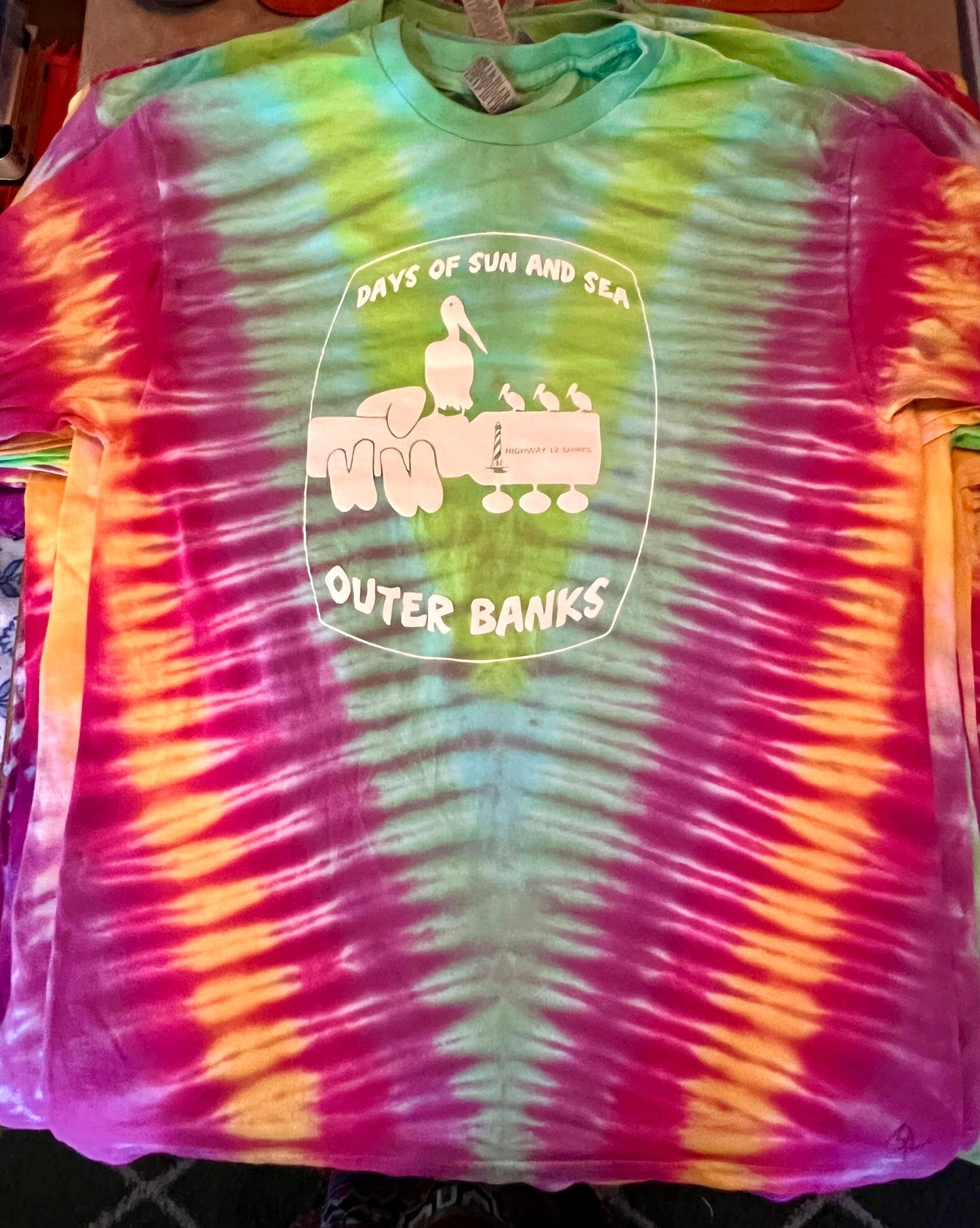 A tie-dye shirt with a graphic that includes text 'Days of Sun and Sea' and ' Outer Banks'. The shirt has a swirling pattern of blue and purple.